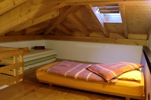 Ein kleines Schlafzimmer im Dachgeschoss mit einem Einzelbett, einer hölzernen Bank und einer geneigten Decke.