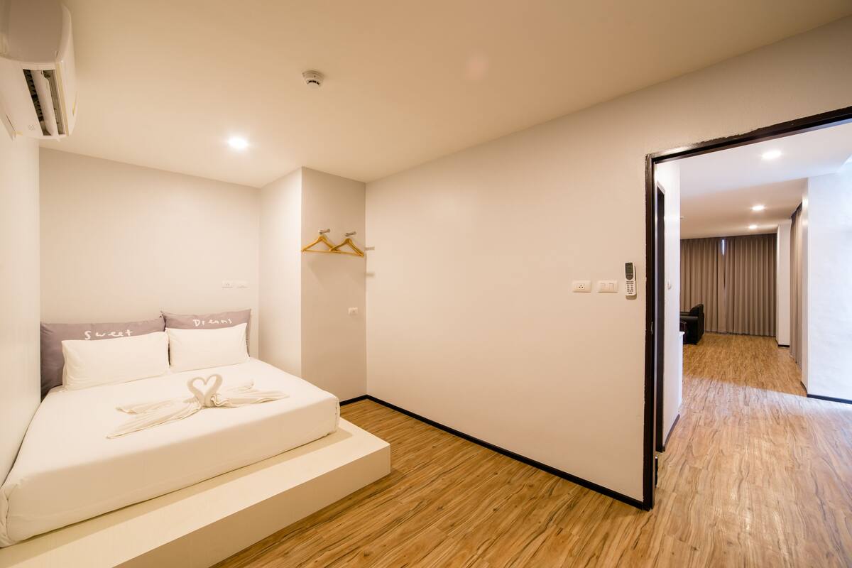 A modern hotel room with a bed, a wooden floor, a wardrobe, and a door leading to another room.