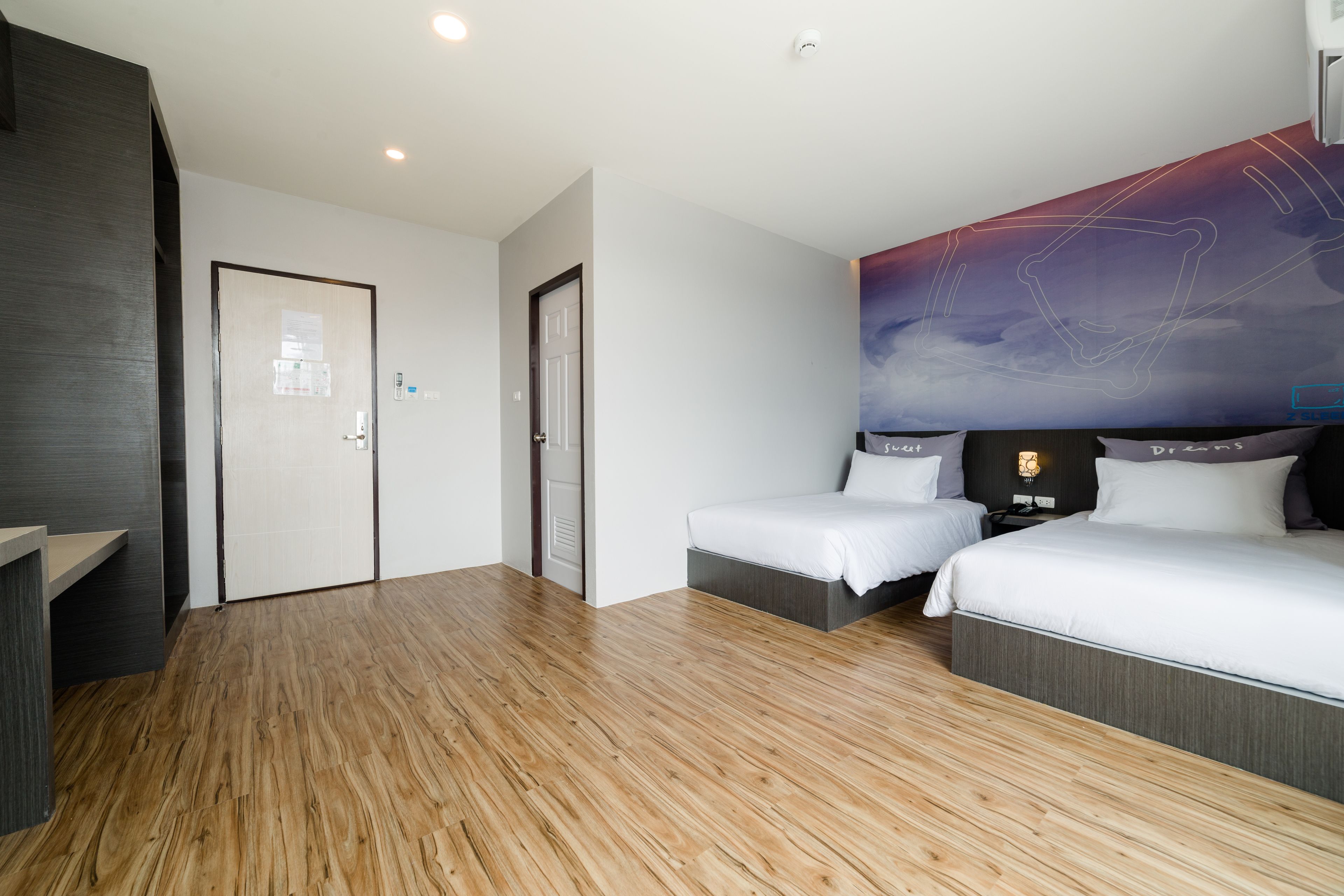 A modern hotel room with two single beds, a wooden floor, a large abstract wall art, and a small desk.