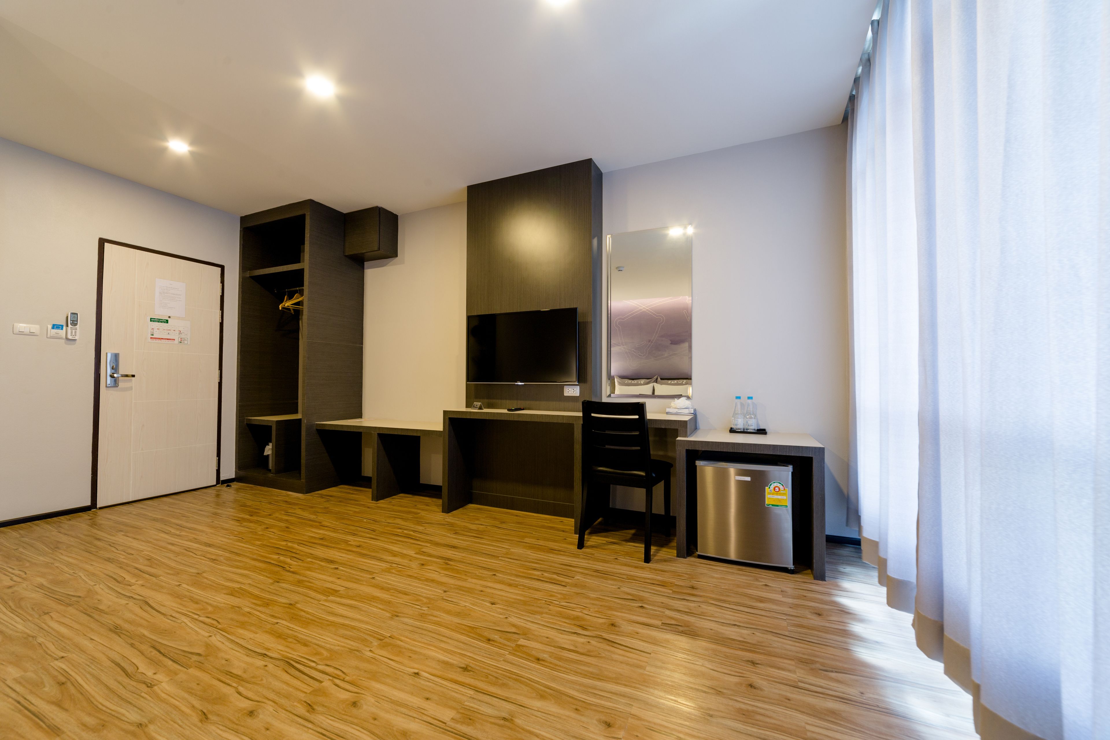 Una habitación de hotel moderna con suelo de madera, un escritorio con silla, una kitchenette pequeña y una cama.