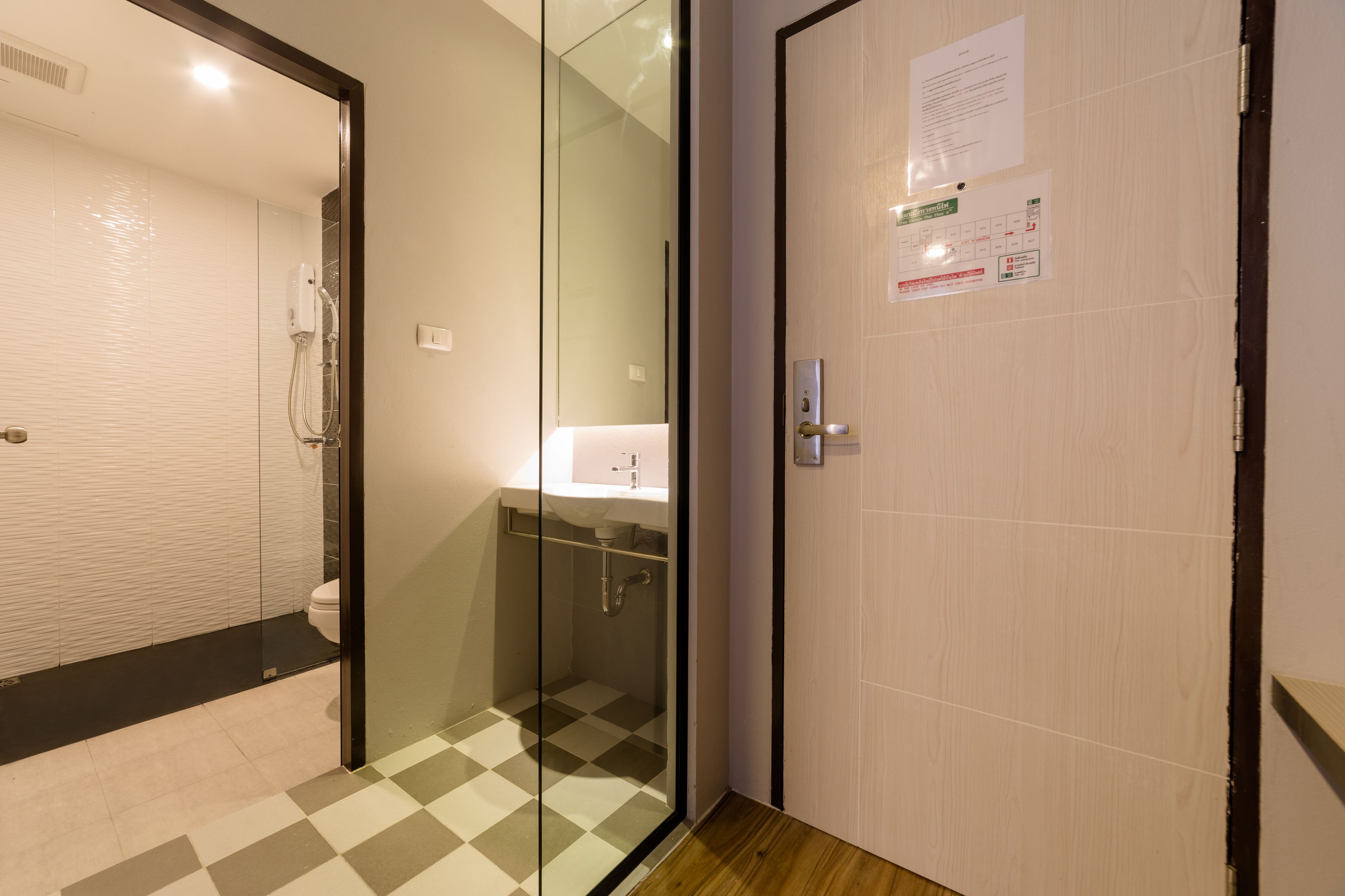 A hotel bathroom with a glass-enclosed shower, a sink, and a door with informational notices.