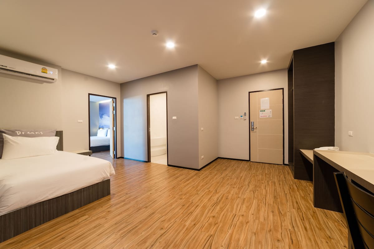 A modern hotel room with a wooden floor, a bed, a desk, and a bathroom.