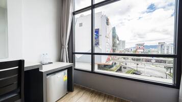 Camera d'albergo moderna con una grande finestra vista città, angolo cottura compatto e piccolo salotto.