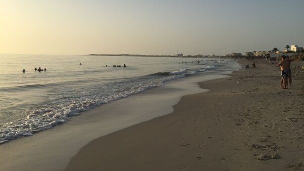 Una playa con gente nadando y caminando por la orilla.