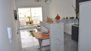 Una cocina moderna con encimera de mármol, un comedor con mesa y sillas, un refrigerador y vistas al balcón exterior.