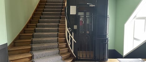 En trappe med gulvbelagte løbere, gelænder i metal og en sort metalport øverst.