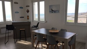 Een eetgedeelte met een houten tafel en stoelen, een bargedeelte en grote ramen met uitzicht op het strand.