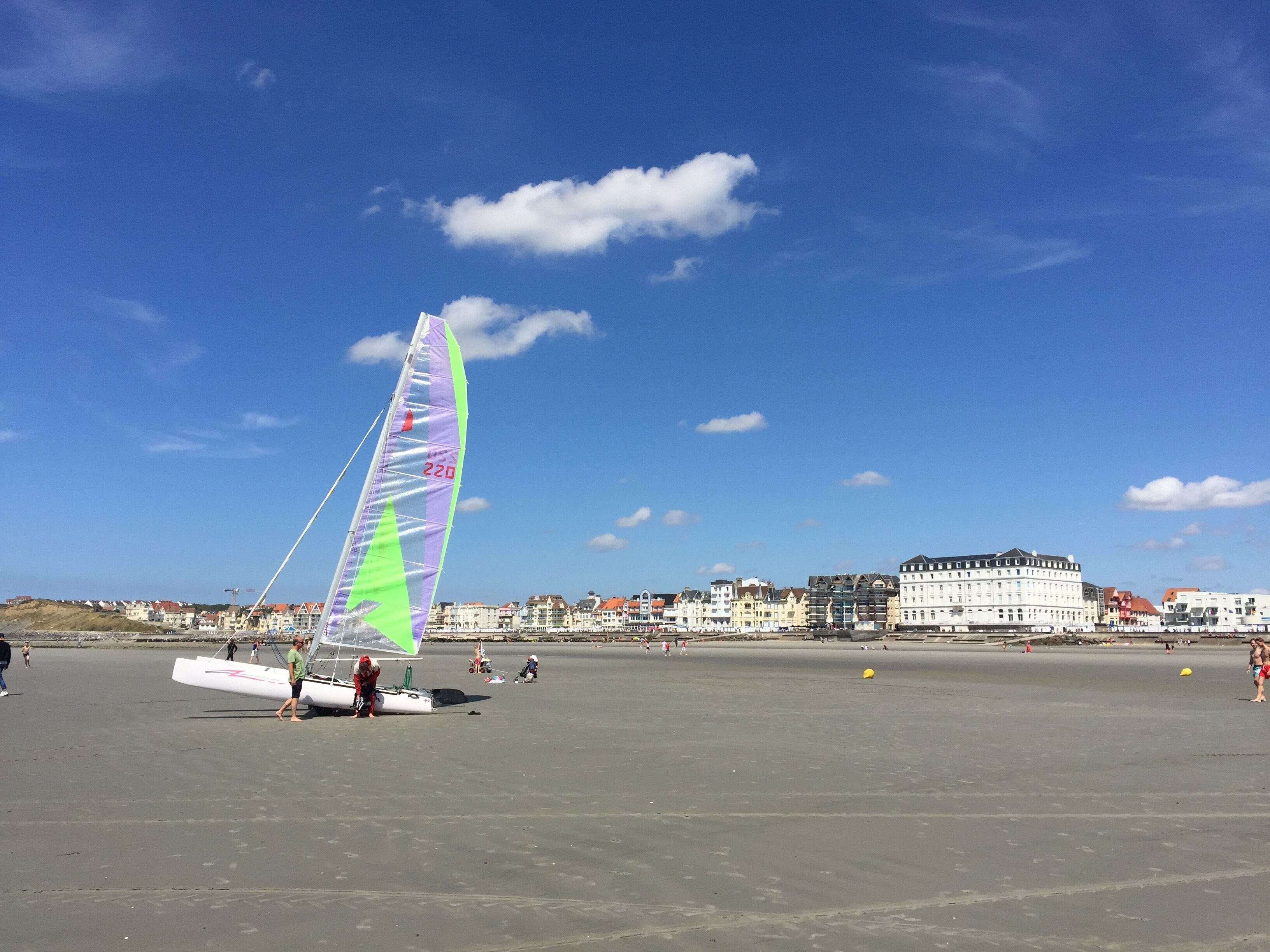 Une plage avec un voilier et un grand bâtiment en arrière-plan.