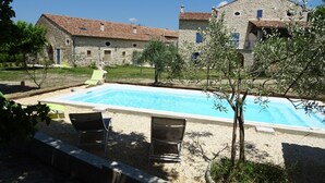 Una piscina con dos sillones de descanso, rodeada de grava y un edificio de piedra con techo de tejas.