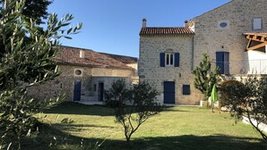 Un edificio de piedra con techo de tejas, un pequeño jardín y un árbol en primer plano.