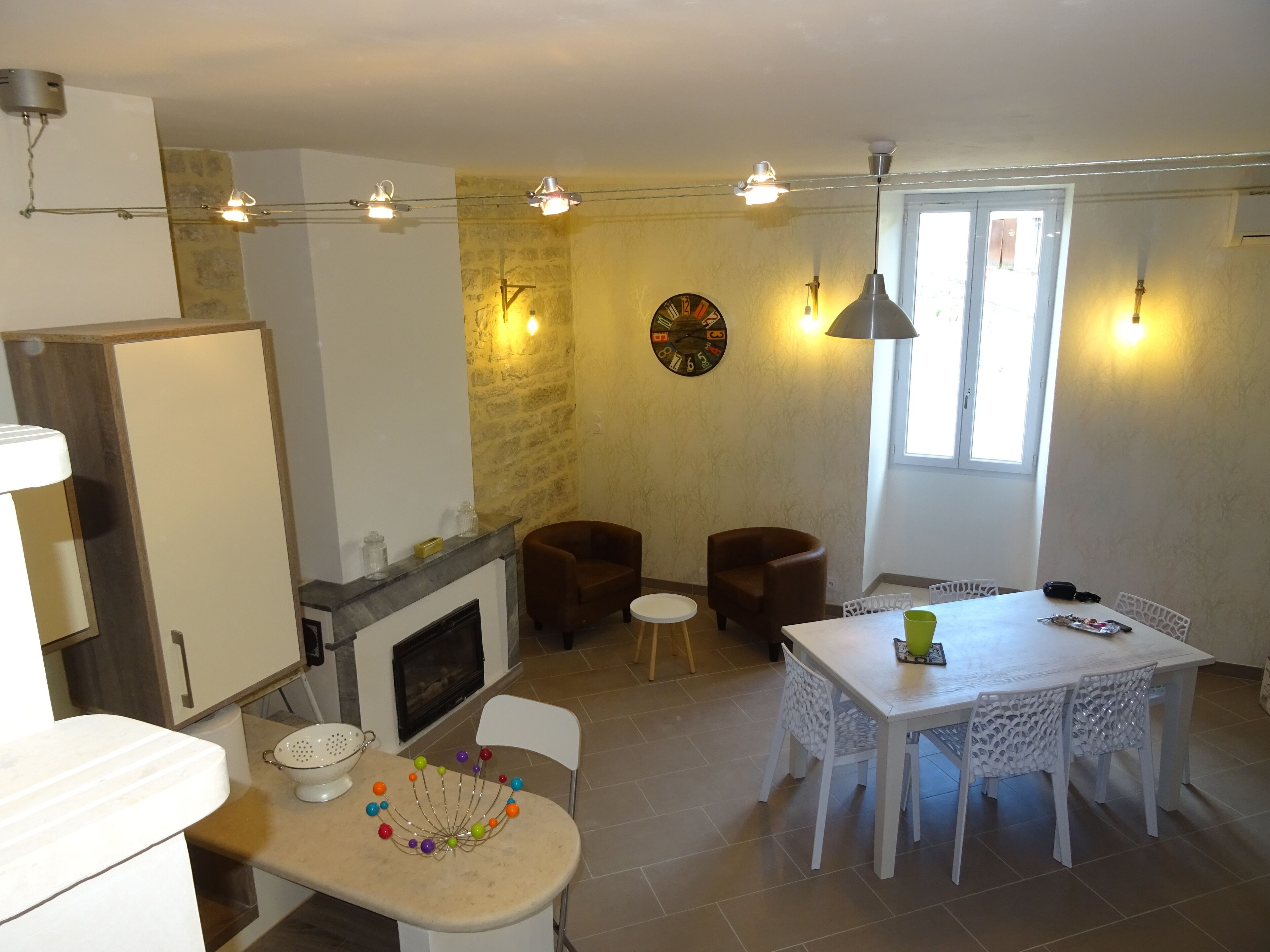 A dining area with a white table and chairs, a fireplace, and a clock on the wall.
