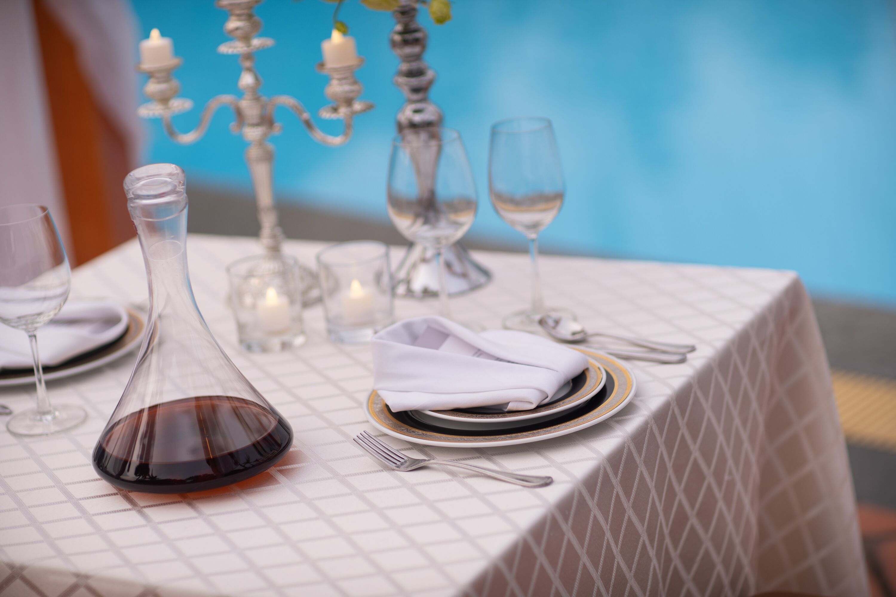 Une table dressée avec des serviettes blanches, un verre à vin, une carafe et une bougie.