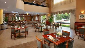 Ein geräumiger Hotel-Speisesaal mit mehreren Tischen und Stühlen, ein Balkon mit Geländer und große Fenster mit Blick ins Freie.