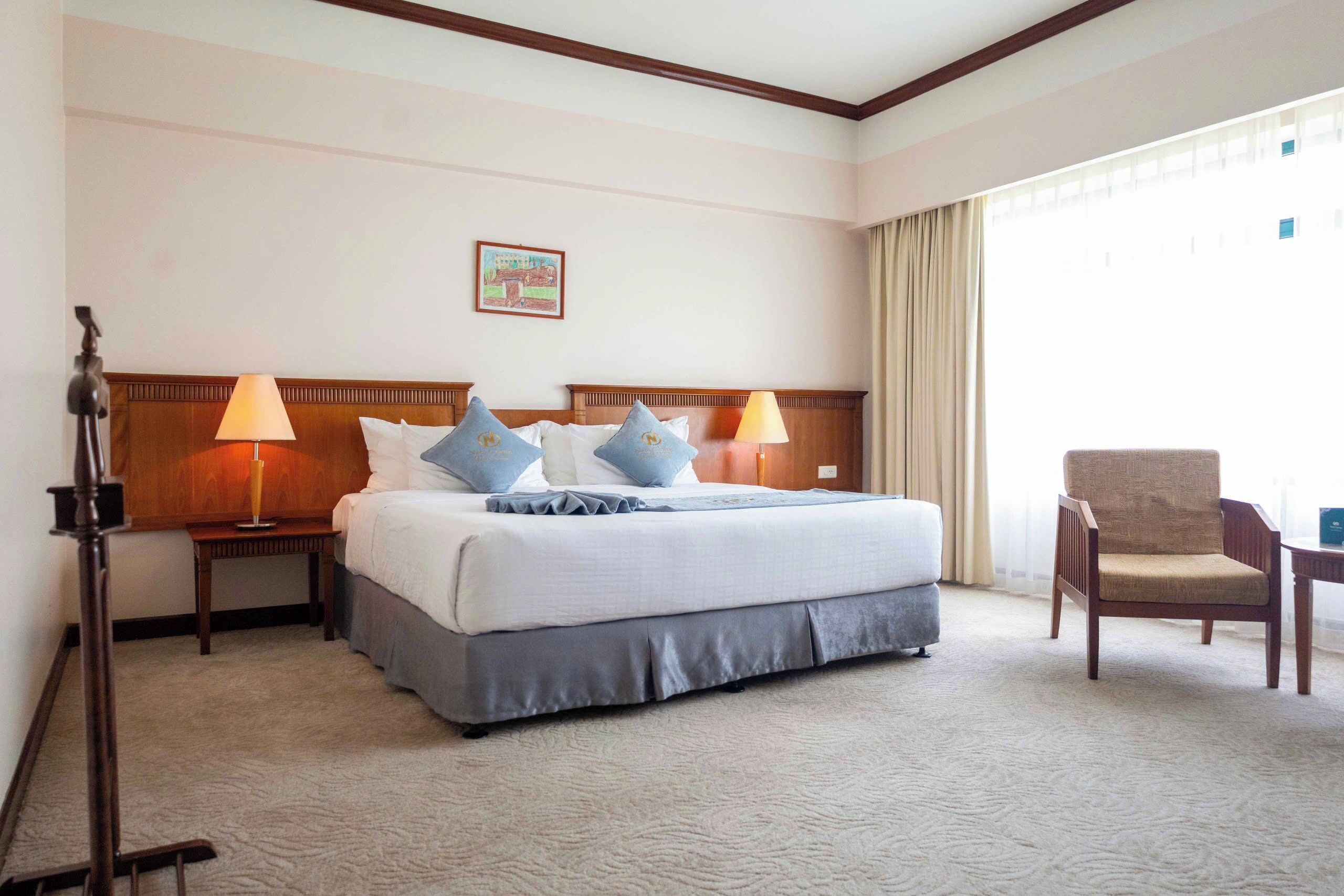 A hotel room with a large bed, two bedside tables with lamps, a chair, and a window with curtains.