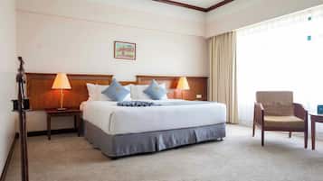A hotel room with a large bed, two bedside tables with lamps, a chair, and a window with curtains.