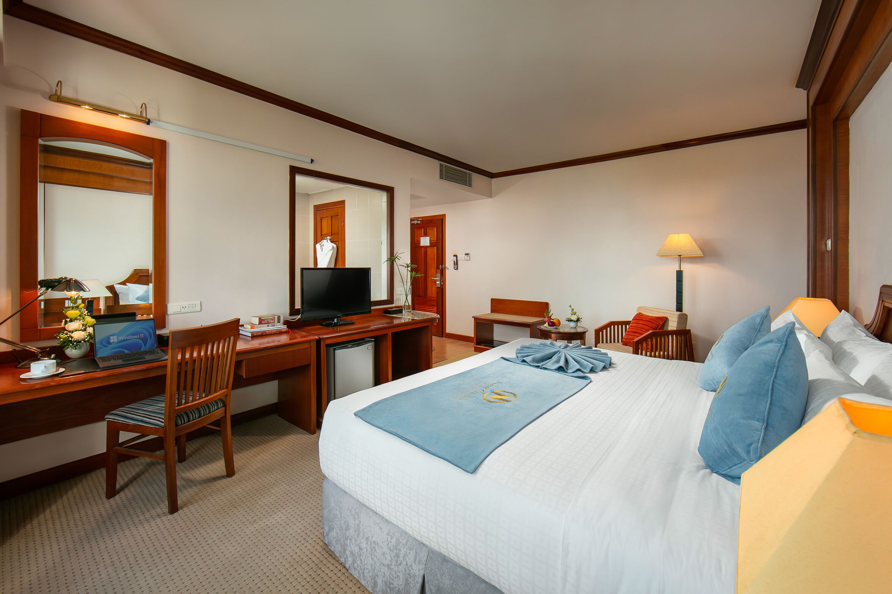 Een hotelkamer met een bed, bureau, stoel, televisie en een lamp.