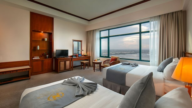 Ein Hotelzimmer mit zwei Betten, einem Schreibtisch, einem Fernseher und einem großen Fenster mit Aussicht.