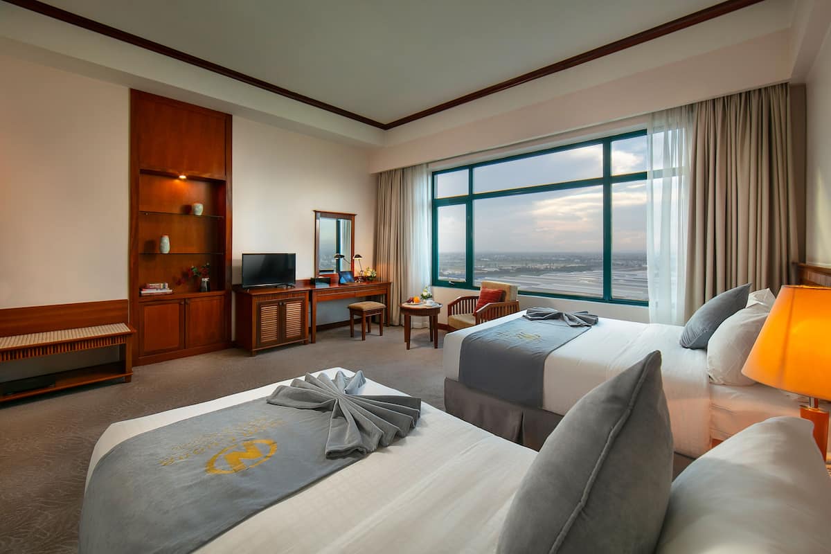 A hotel room with two beds, a desk, a TV, and a large window with a view.