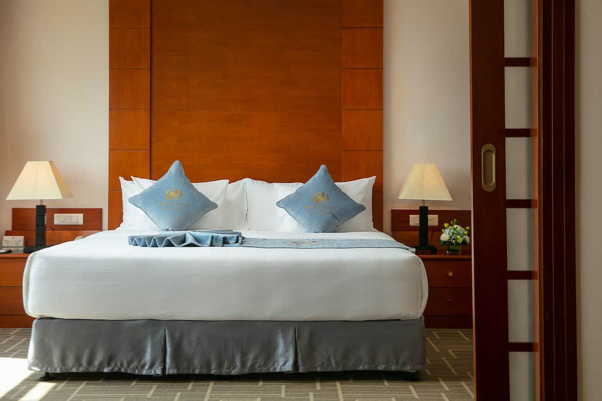 A neatly made bed with a wooden headboard, two bedside lamps, and a nightstand with a vase of flowers.