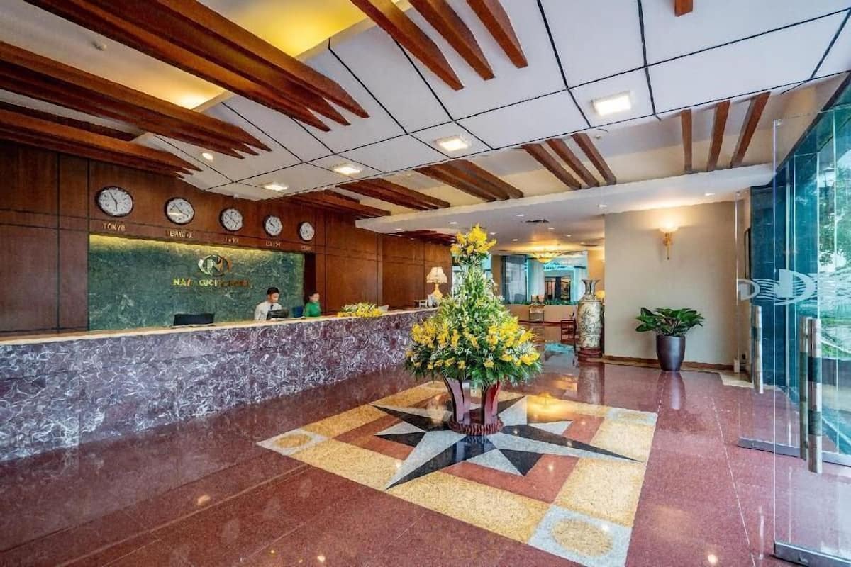 A hotel reception area with a marble counter, wooden ceiling beams, clocks, and a flower arrangement.