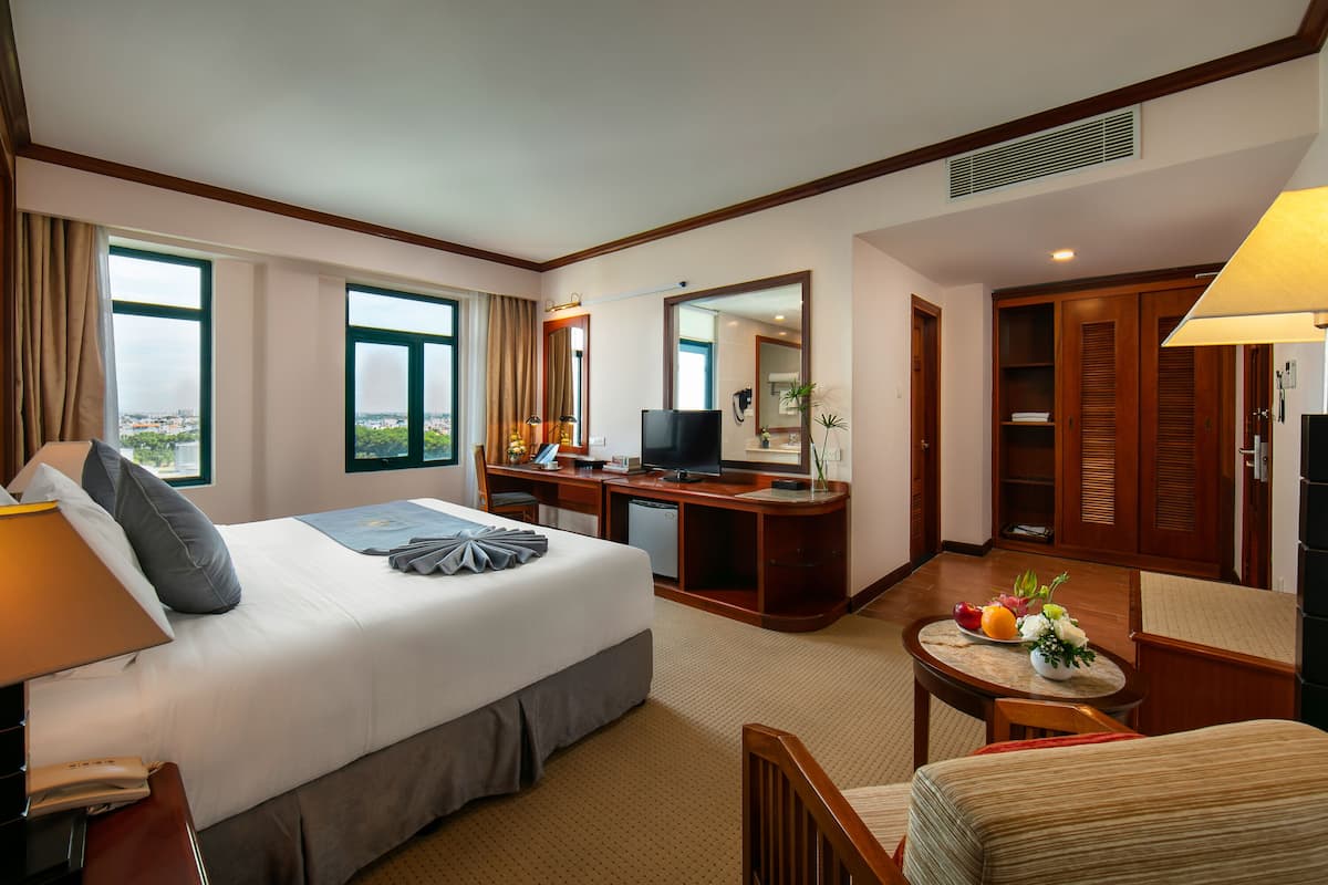 A hotel room with a bed, desk, chair, and a small table with a fruit bowl.