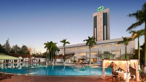 Ein Hotel mit Swimmingpool, Palmen und einem hohen Gebäude mit einem Logo.