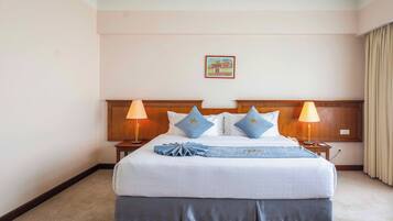 A hotel room with a large bed, two bedside lamps, a headboard with a logo, and a small painting on the wall.