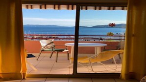 Un balcon offrant une vue sur la mer et les montagnes lointaines, avec une table et des chaises.