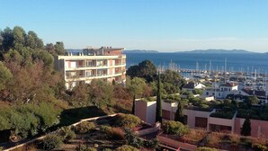 Un immeuble à plusieurs étages, doté de balcons, entouré de verdure et offrant une vue sur une marina où sont amarrés des bateaux.