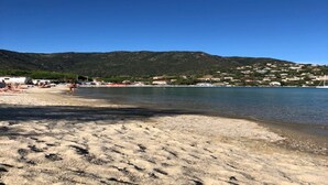 Une plage avec une eau d’un bleu limpide, un rivage sablonneux et une chaîne de collines en arrière-plan.