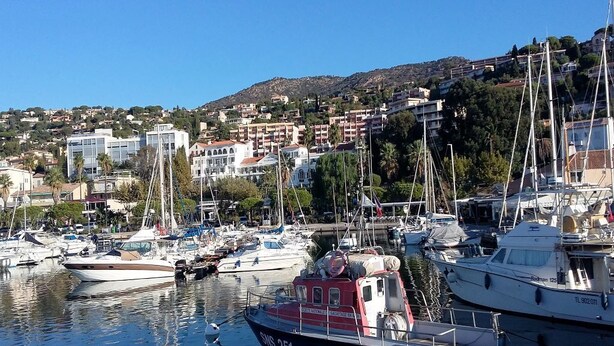 Un port de plaisance où sont amarrés des bateaux, entouré d’immeubles résidentiels et de collines.
