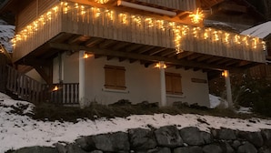 Eine Holzhütte mit Balkon, Stein Fundament und verschneitem Gelände.