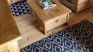 Ein gemütliches Wohnzimmer mit Holzboden, zwei Ledersofas mit Kuhhautkissen, einem Holztisch mit Blumenvase, einem Holzschrank und einem an der Wand befestigten Spiegel.