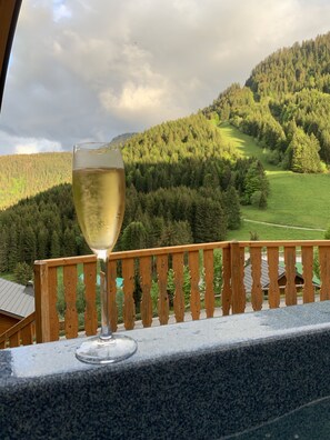 Ein Glas Weißwein auf einem Balkon mit Blick auf einen bewaldeten Berg.
