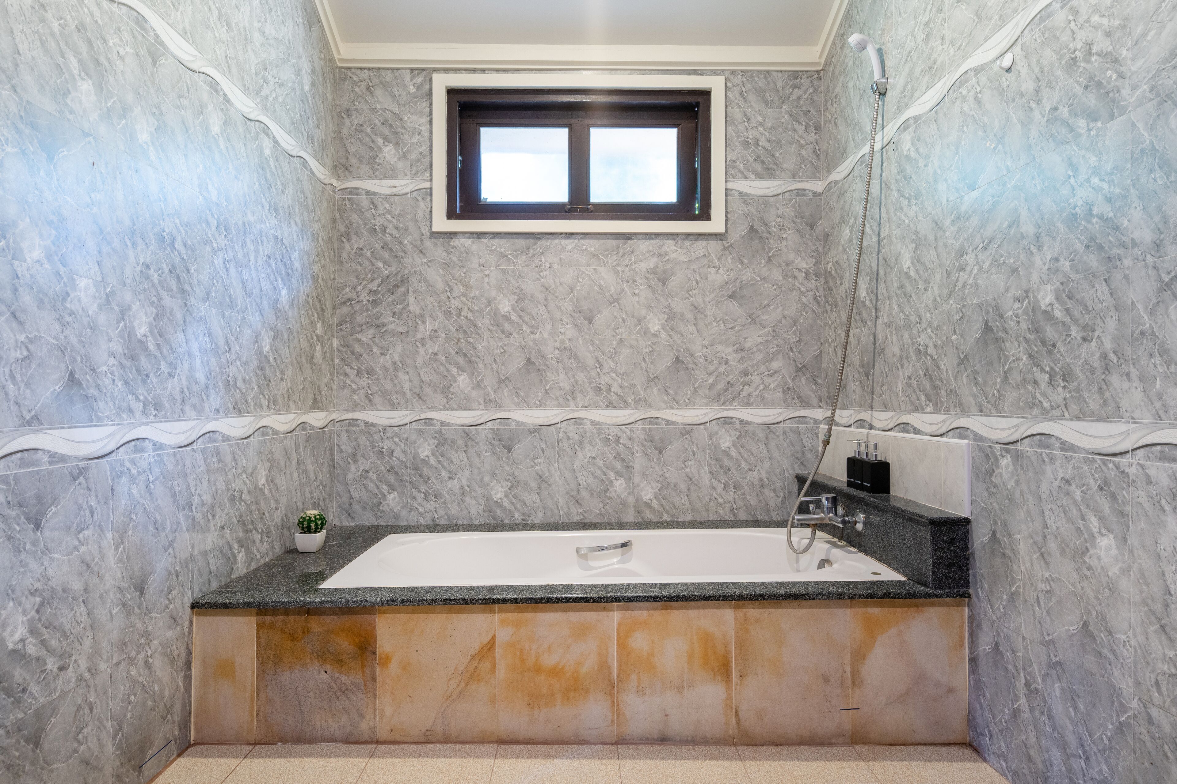 Une salle de bain avec un mur en marbre, une fenêtre, une baignoire et une douche.