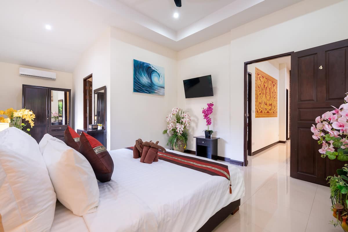 A hotel room with a large bed, a flat-screen TV, a decorative wall piece, and a door with a number.
