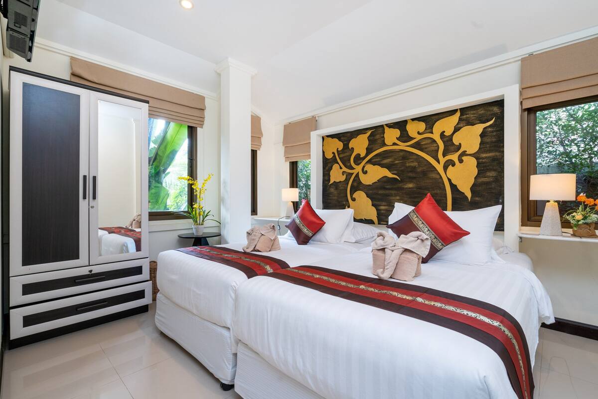 A hotel room with two beds, a wardrobe, a large mirror, and a decorative wall piece.
