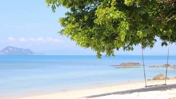 Une plage avec une eau d’un bleu limpide, un rivage sablonneux et un arbre qui offre de l’ombre.