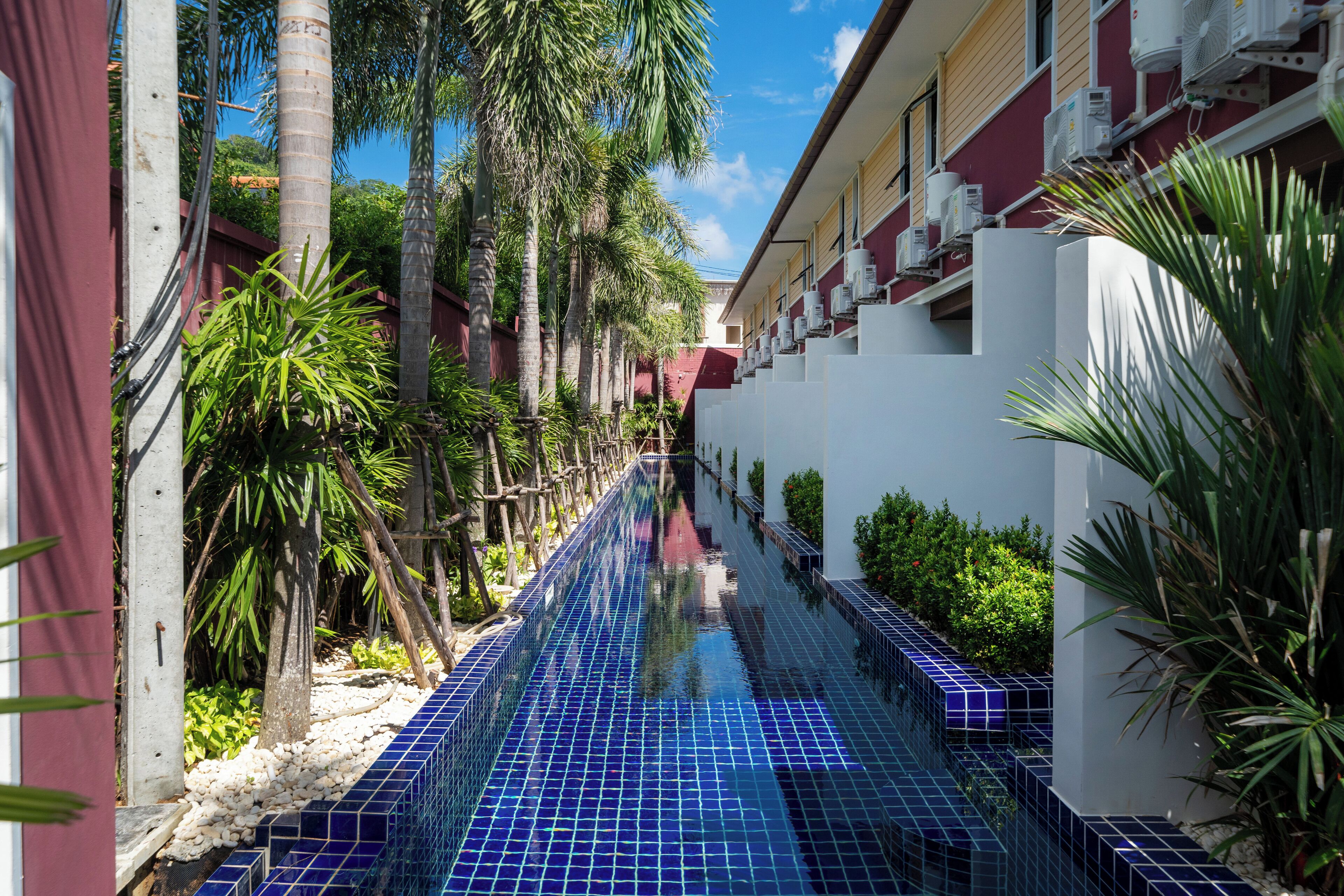 A narrow, tiled waterway flanked by palm trees and a building with air conditioning units.