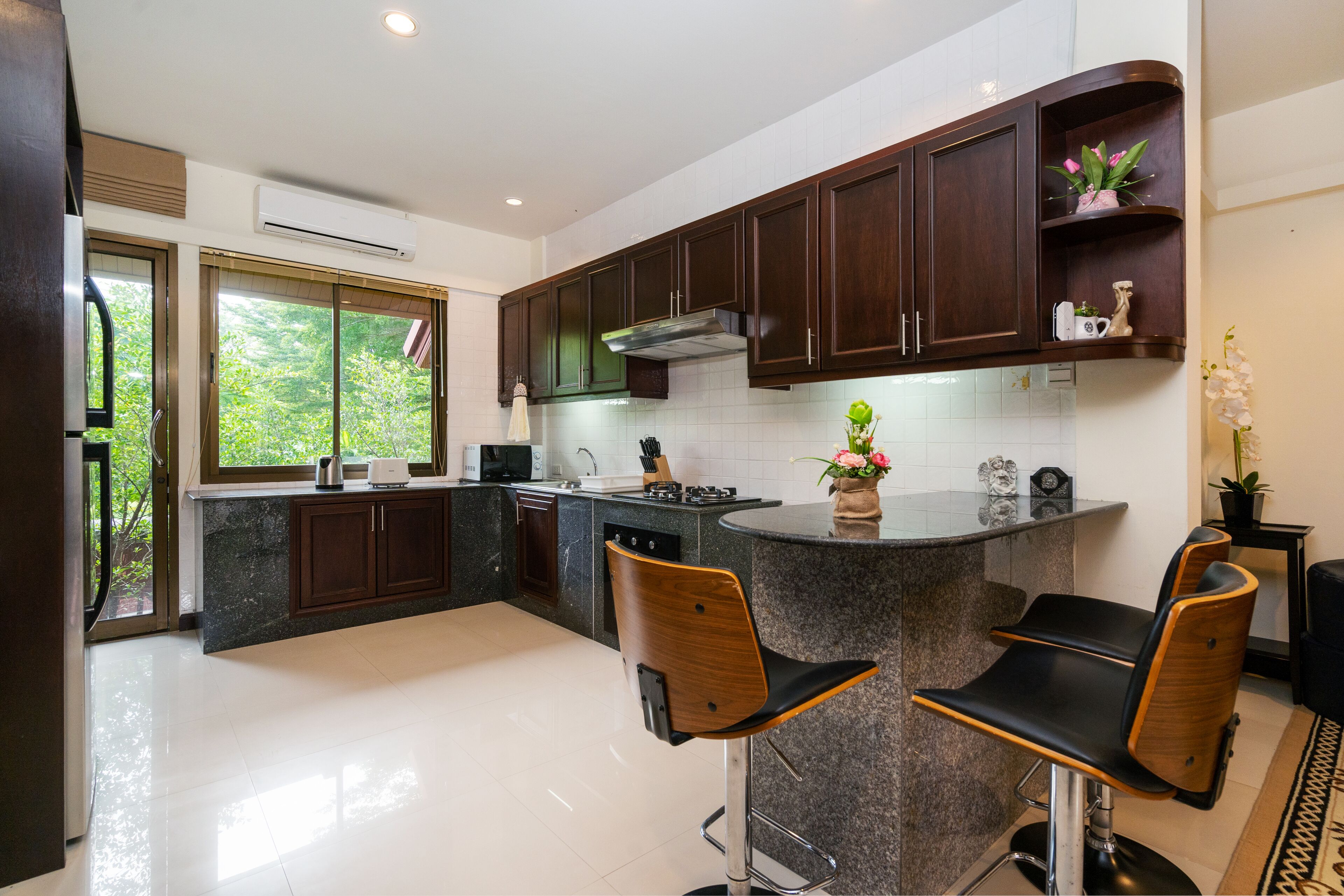 A modern kitchen with dark wooden cabinets, a granite countertop, and a bar area with two bar stools.