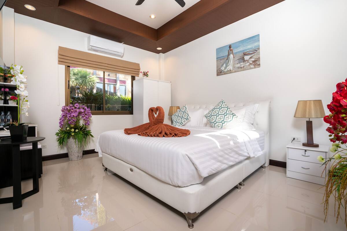 A bedroom with a bed, bedside table, lamp, and a window with a view of the outside.