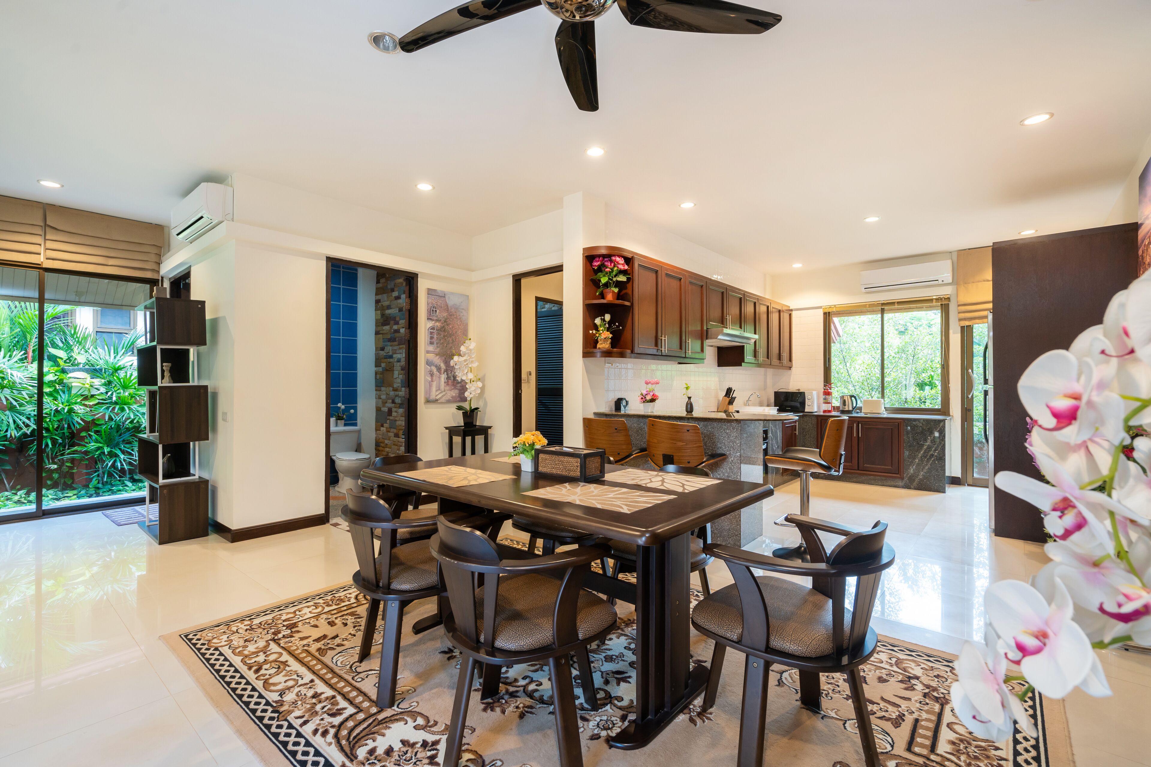 A modern kitchen with dark wooden cabinets, a central island, and a dining area with a table and chairs.