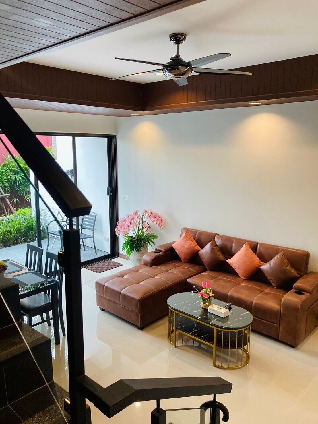 A modern living room with a brown leather sofa, a glass coffee table, and a ceiling fan.