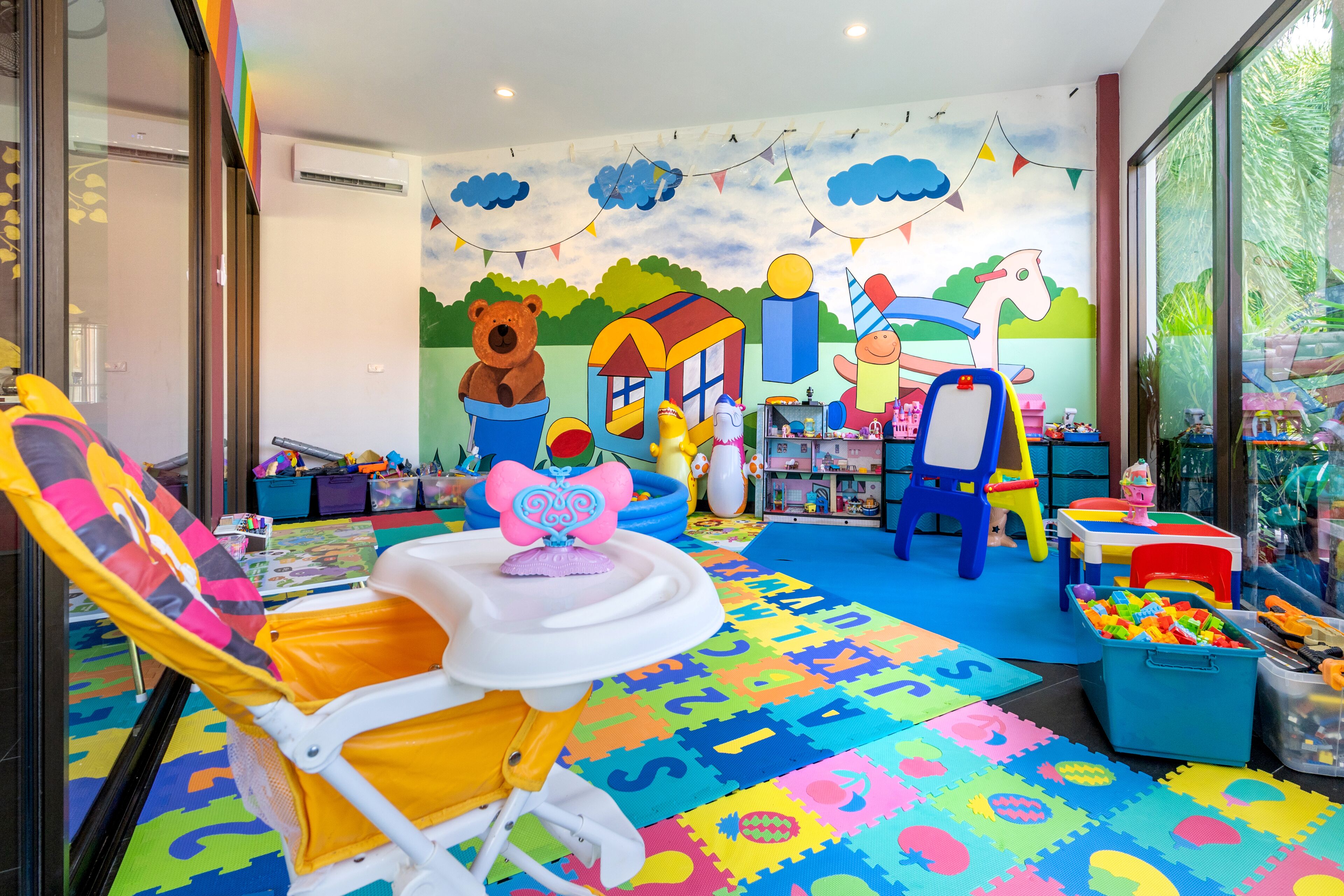 Una sala de juegos infantil con colchonetas coloridas, juguetes y un mural.