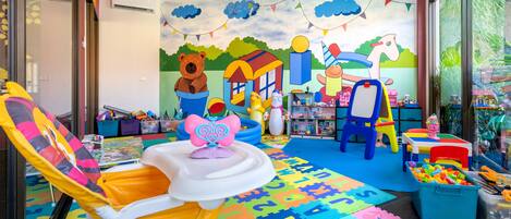 Una sala de juegos infantil con colchonetas coloridas, juguetes y un mural.