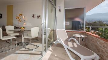 A balcony with a glass door, a dining area with a table and chairs, and a lounge chair.