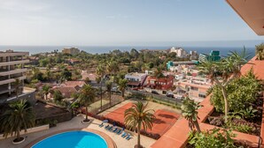A pool area with lounge chairs and palm trees, overlooking a coastal town with buildings and a view of the sea. - Apartment with fantastic panoramic views to the Teide and the sea, balcony facing west (Puerto de la Cruz)
