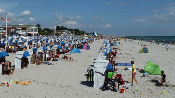 Ein Strand mit vielen Zelten, Strandliegen, einem Spielplatz und einem klaren Himmel.