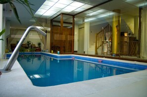 Una piscina interior con agua cristalina y azul, rodeada por paredes de vidrio y columnas de madera.
