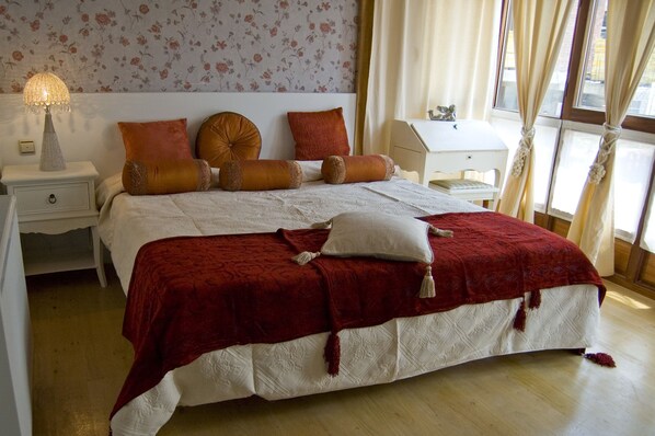Una cama bien hecha con una colcha roja, dos almohadas y una lámpara decorativa sobre una mesita de noche.